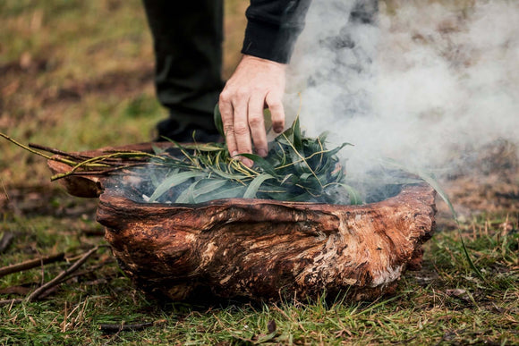 Photo of a person's hand placing leaves on a fire for a smoking ceremony. 